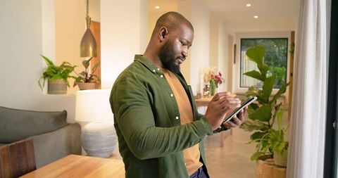 African American man using tablet in modern living room with indoor plants and warm decor