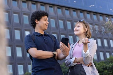 African american young professionals sharing smartphone, smiling and talking in urban plaza
