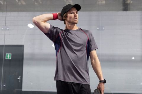 Young athlete standing in gym holding weight plate wearing cap wristband fitness watch
