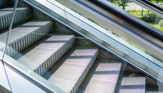 Glinting Ribbed Escalator Steps Casting Parallel Shadows, Glass Balustrade Detail