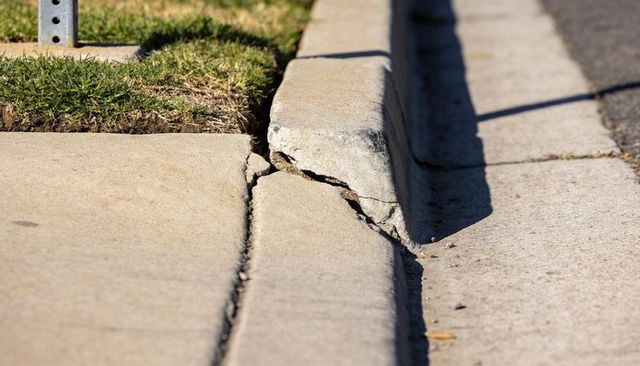 Cracked concrete curb fractured sidewalk slab close-up showing pavement damage