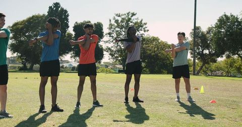 Diverse male athletes stretching arms across chests on grassy field during team warm-up