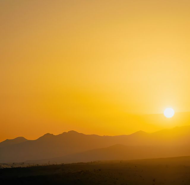 This serene image shows a golden sunrise casting warm light over a mountain range. Perfect for travel websites, outdoor adventure blogs, posters promoting relaxation and tranquility, and environmental awareness campaigns.