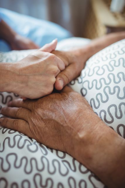 Close-up of nurse holding hands of senior woman in bedroom