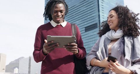 Diverse young professionals collaborating on tablet and smartphone by glass tower rooftop