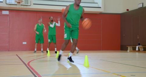 Diverse male basketball players dribbling through cones in agility ball-handling drill