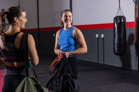 Female training partners packing gym bag after boxing workout, smiling and chatting