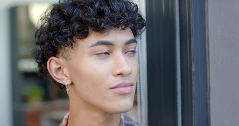 Young man wearing cross earring looking contemplative by storefront window, close-up