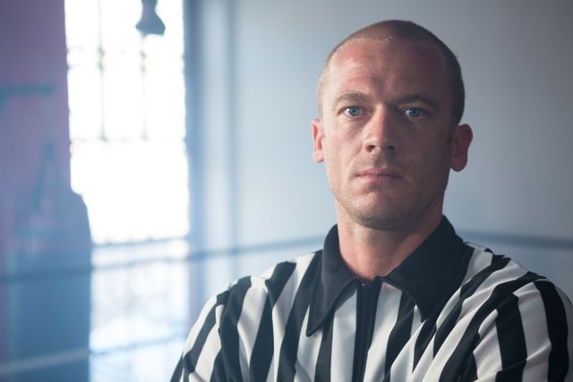This image captures a serious male referee standing in a boxing ring, wearing a striped shirt. Ideal for use in sports-related articles, promotions for boxing events, or materials discussing sports officiating and authority figures in athletics.