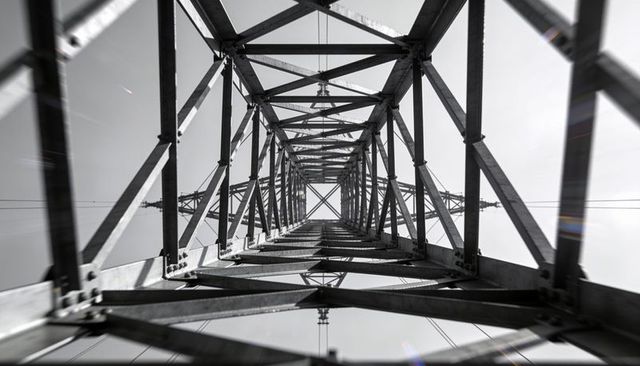 Upward view steel transmission tower lattice geometry high-voltage power lines monochrome