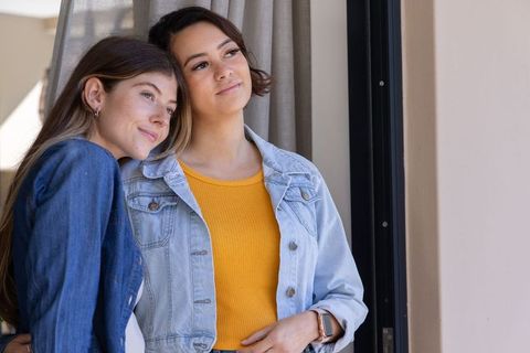 Young women leaning on shoulder sharing quiet moment by doorway in denim jackets