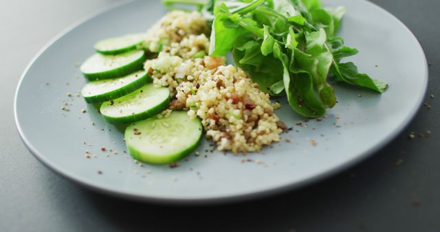 Image of fresh sliced cucumber, leaves and grains salad on grey plate over dark grey background. fusion food, fresh vegetables and healthy eating concept.