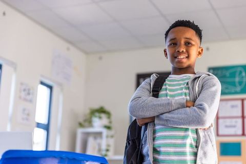 Confident african american school-age boy standing in classroom carrying backpack smiling