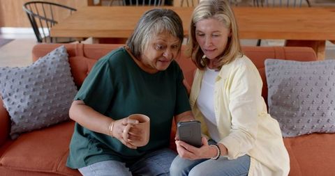 Diverse female friends enjoying smartphone at home