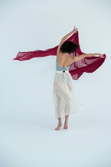 Dancer practicing contemporary dance with red fabric in a studio. Ideal for use in articles or advertisements related to dance, performing arts, fitness, and creative expression. Can also be used in educational materials about dance techniques and choreography.
