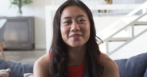 Smiling Asian woman sitting on gray sofa in bright modern living room interior