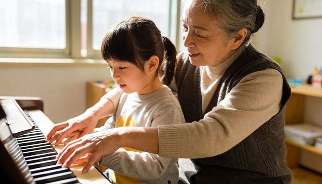 Grandmother guiding granddaughter on upright piano keys for intergenerational music lesson
