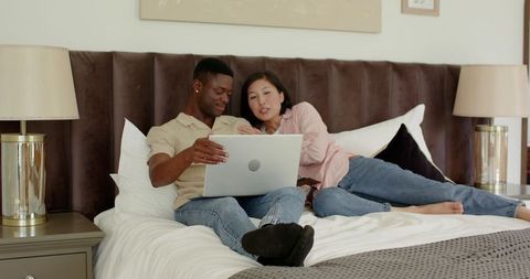 Couple relaxing on bed with laptop for online shopping experience