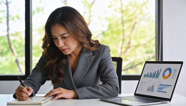 Asian professional reviewing laptop charts, writing notes and planning business strategy