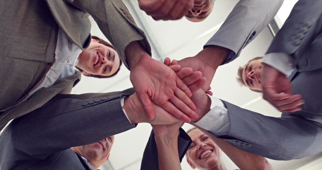 A diverse group of business professionals stacks their hands together in a gesture of teamwork and unity, with copy space. Their smiling faces, seen from below, convey a sense of accomplishment and collaboration.