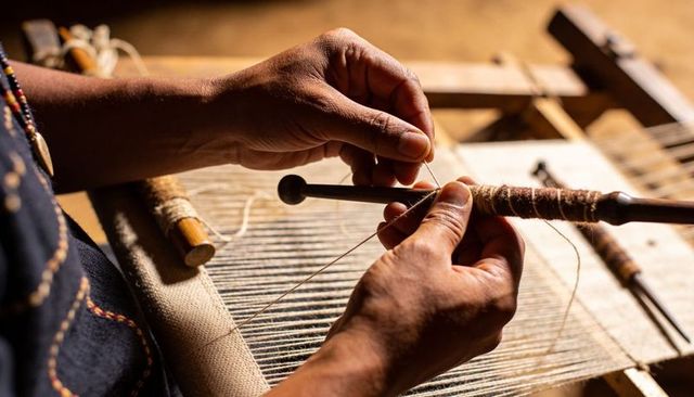 Artisan hands weaving on traditional wooden loom holding shuttle wrapped with yarn