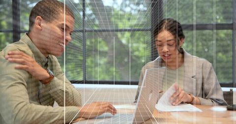 Collaborating with laptop and documents in glass office with digital grid overlay
