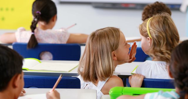 Two Young Schoolgirls Whispering in Classroom During Lesson - Download Free Stock Images Pikwizard.com