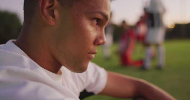 Image of sad biracial football player siting on field. Male football team, inclusivity and fitness in team sports.