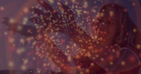 Smiling woman raising arms into warm bokeh light overlay in cozy living room lifestyle portrait