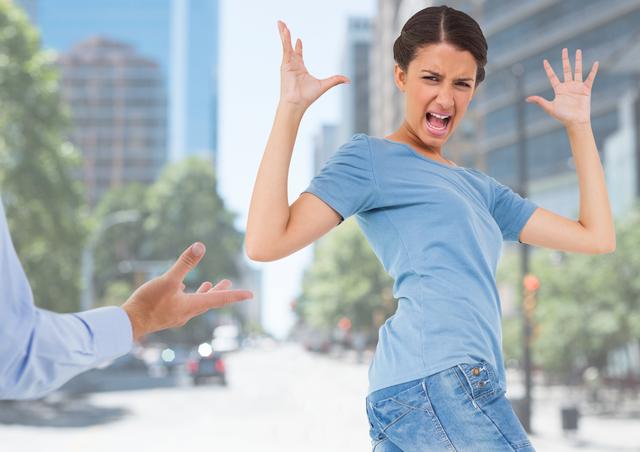 Young woman expressing frustration and anger in an urban environment with city buildings in the background. Ideal for illustrating concepts of stress, conflict, emotional outbursts, and urban life challenges. Can be used in articles, blogs, and advertisements related to mental health, stress management, and urban living.