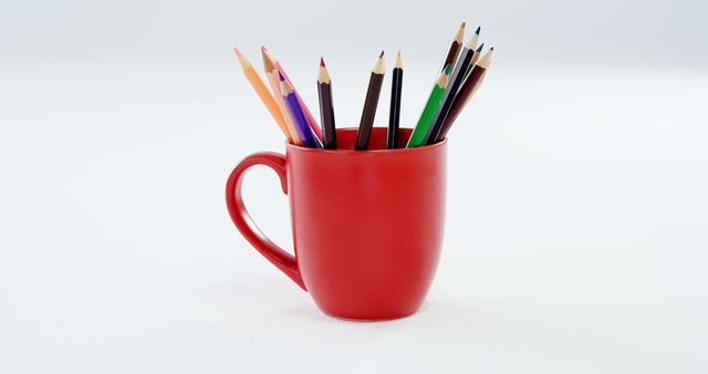 A red mug filled with a variety of colored pencils is positioned against a white background, with copy space. Ideal for themes related to art, creativity, or office and school supplies.