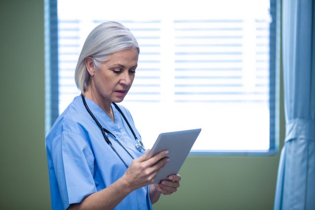 Senior nurse using digital tablet in hospital room, focusing on patient care and medical technology. Ideal for healthcare, medical technology, and nursing-related content. Useful for illustrating modern healthcare practices, digital transformation in hospitals, and professional medical environments.