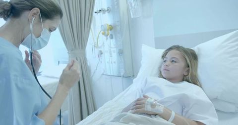 Nurse examining young girl in hospital bed with IV line using stethoscope