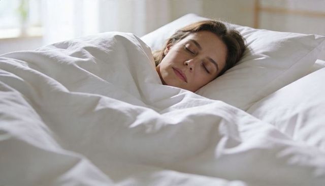 Middle-aged woman sleeping peacefully under white duvet in sunlit minimalist bedroom