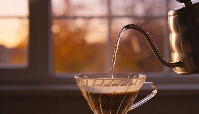 Pouring gooseneck kettle brewing pour-over coffee in glass dripper at golden hour