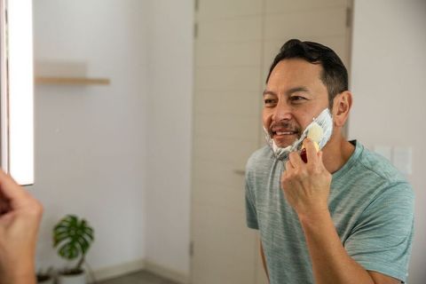 Mature asian man applying shaving cream with brush at bathroom mirror