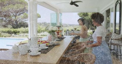 Women arranging tea set and fruit on long counter at poolside patio overlooking garden