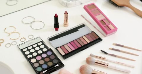 Displaying three open eyeshadow palettes with brushes lipsticks and rings on white vanity