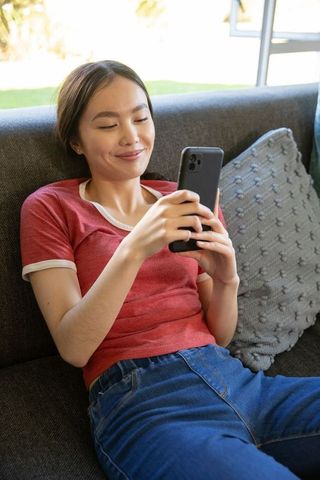 Smiling Young Woman Relaxing on Sofa with Smartphone at Home