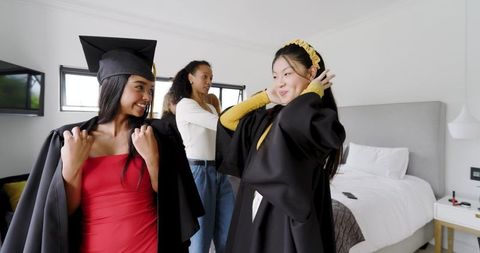 Multicultural friends getting ready for graduation wearing gowns and mortarboards