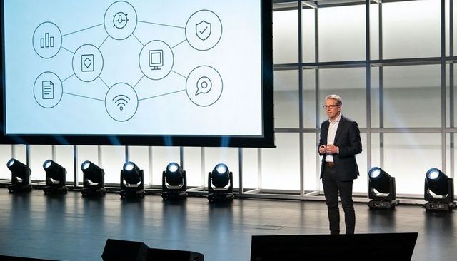 Business leader presenting keynote on stage with network diagram projection and stage lights