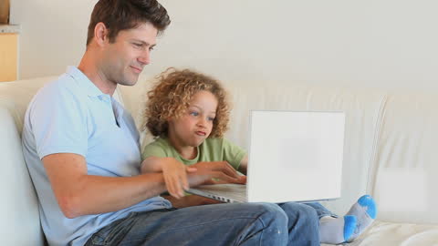 Father and Son Together on Sofa Using Laptop