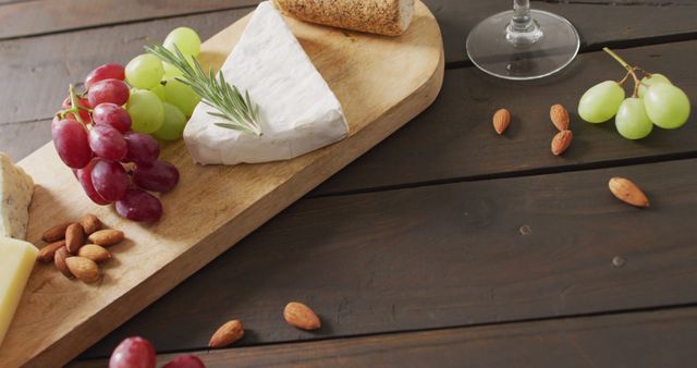 Image of cheeses, bread, grapes and nuts on board and wine glass on wooden table, with copy space. quality light food snack and drink.