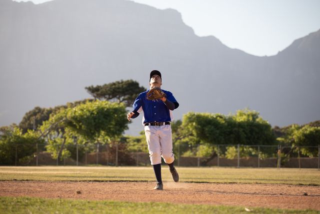 Biracial male baseball fielder during a game in baseball field on a sunny day, running wearing glove. Baseball sports competition.