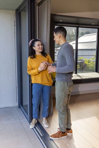 Couple sharing morning coffee in sliding door wearing cozy sweaters and jeans