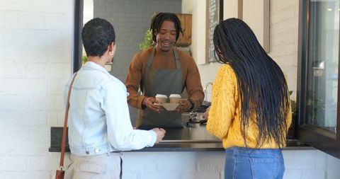 African american barista handing takeaway coffee to customers at cafe window, friendly service