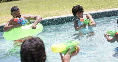 Family Having Fun Playing with Water Guns in Swimming Pool