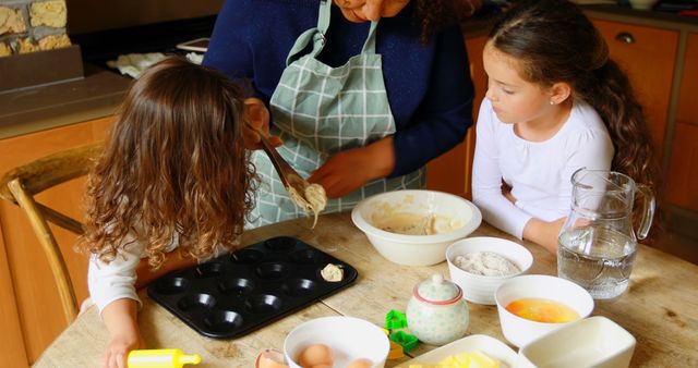 Mother teaching daughters how to bake cookies in home kitchen, demonstrating family bonding and togetherness. Useful for topics of parenting, family activities, home cooking, education, and quality time. Ideal for advertising baking products, family-oriented services, or educational materials on child development and teamwork.