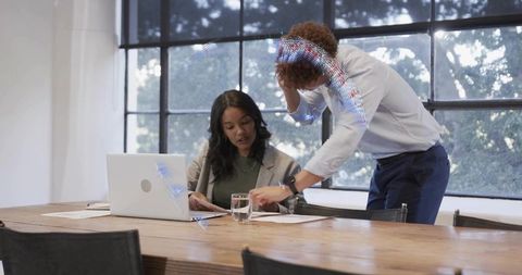 Business colleagues collaborating over documents at sunlit office table with laptop