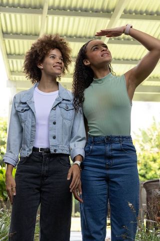Two african american friends standing under canopy smiling and looking up in casual denim